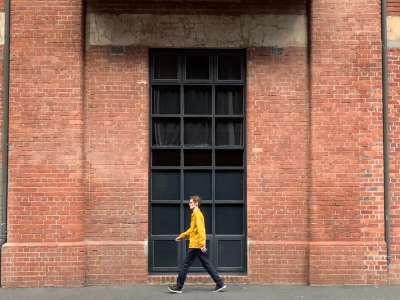 man wearing yellow coat walking past exterior of brick wall