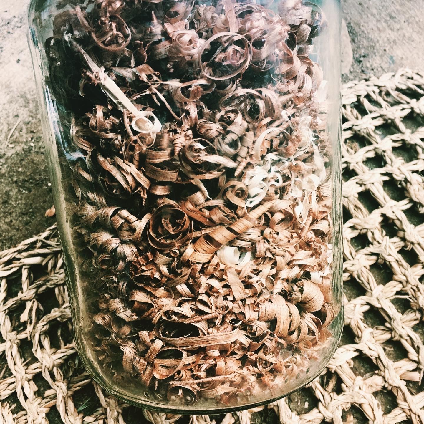 glass jar on a woven mat filled with curly wood shavings. 